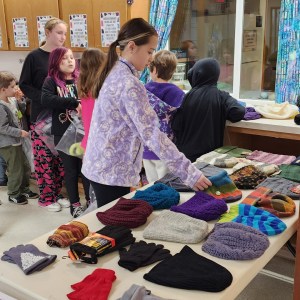 Children are lined up at a table covered in winter hats and gloves.