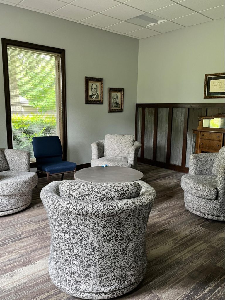 A small seating room with five well-cushioned chairs, a coffee table, and various decorations. Good for a small group to talk.